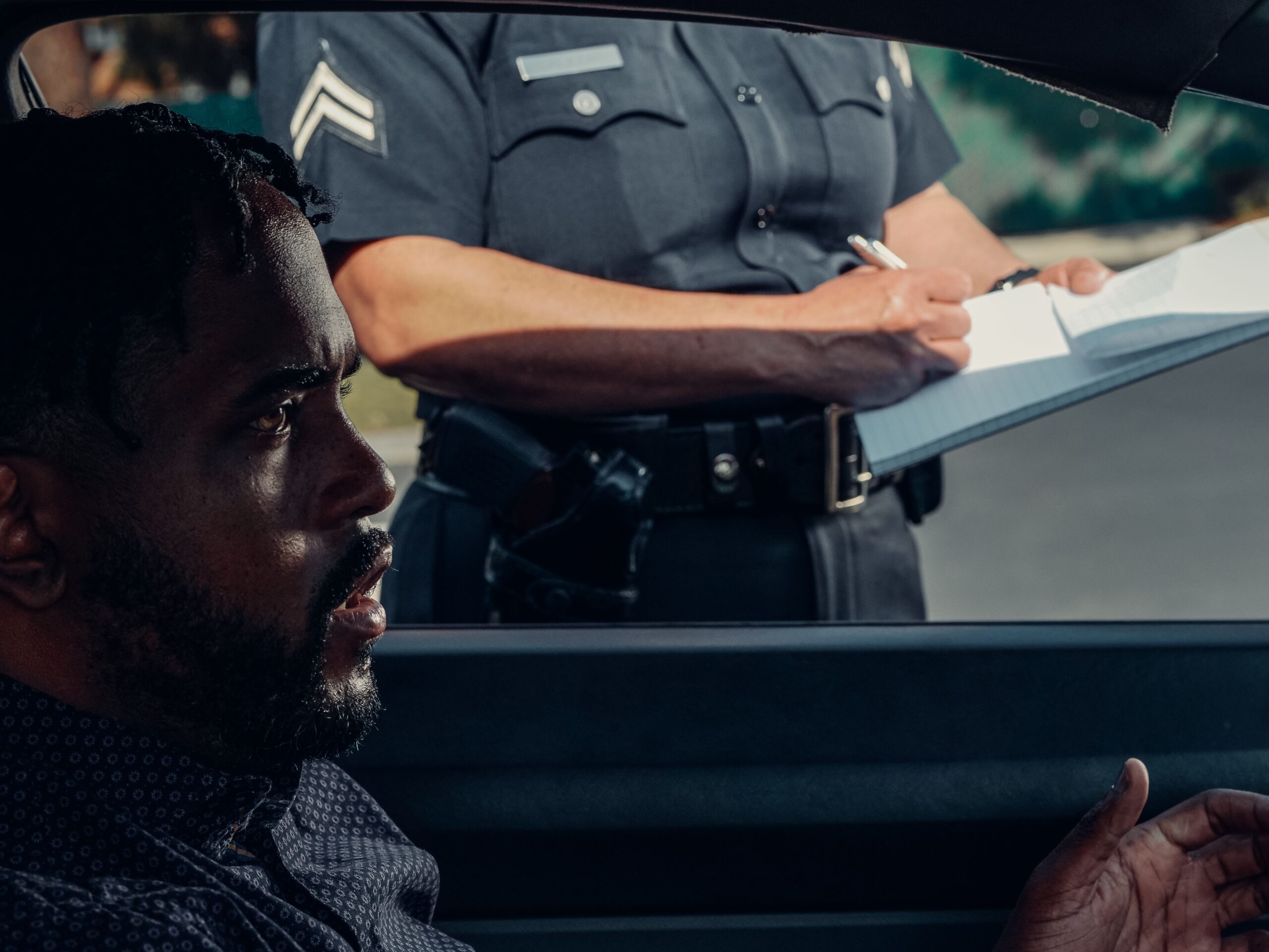 Interior close-up of driver at traffic stop with window down and police officer standing outside driver's window